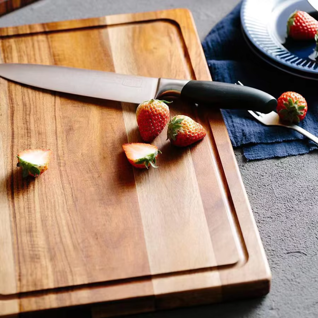 Wooden cutting board with a knife and strawberries on a dark surface