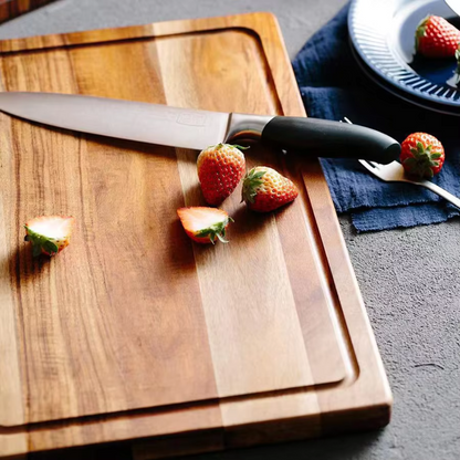 Wooden cutting board with a knife and strawberries on a dark surface