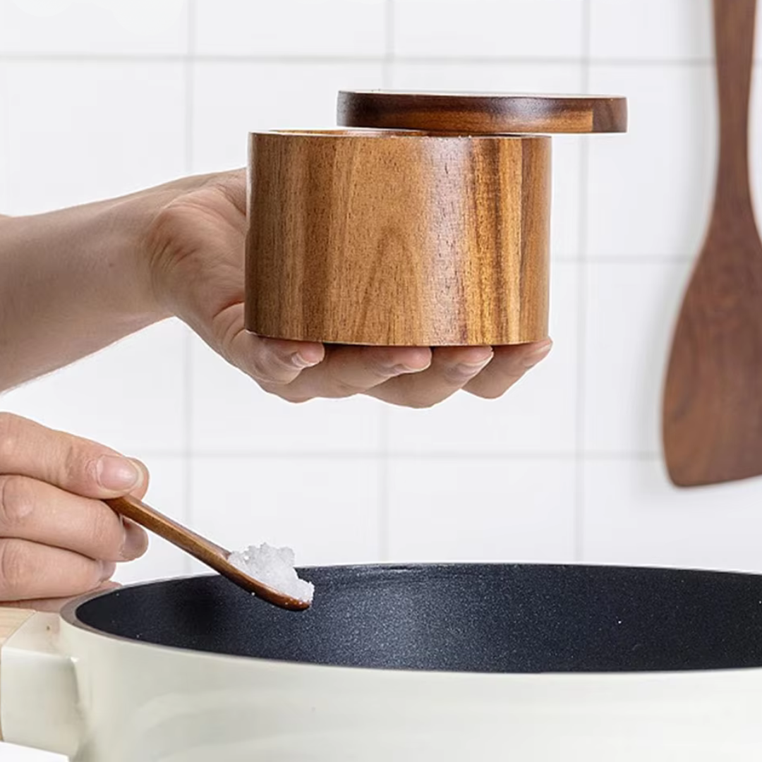 Person adding salt from a wooden salt cellar into a pot.