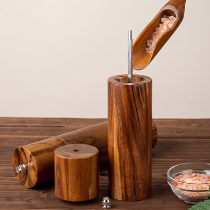 A wooden salt and pepper mill set with a cylindrical wooden body, metal grinding mechanism, and a wooden scoop filled with pink Himalayan salt, displayed on a rustic wooden table.